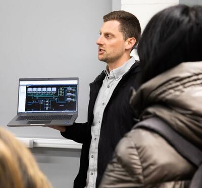 Ross Ruecker holds a computer in front of a group of students.