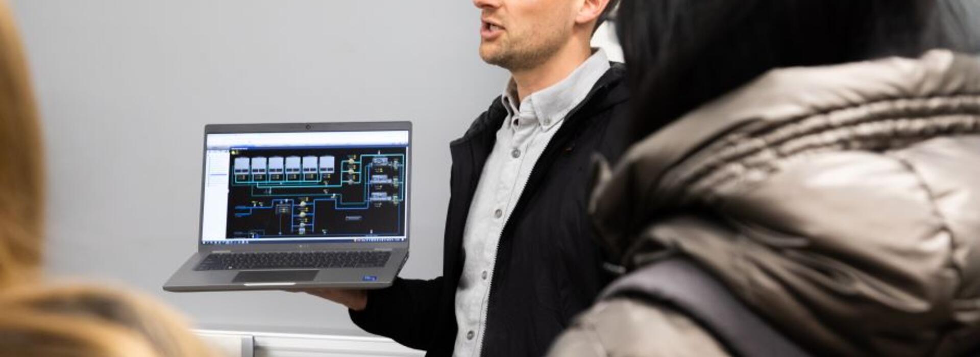 Ross Ruecker holds a computer in front of a group of students.