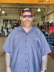 Man with a red beard black hat and blue button down work shirt. 