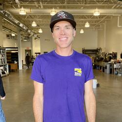 Tim standing in the landscape shop wearing a  black hat and a purple t-shirt