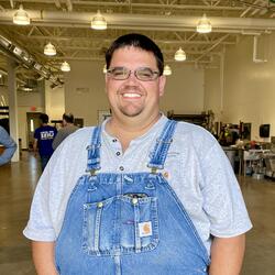 Chris in blue overalls standing in the landscape shop. 