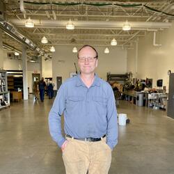 Terry standing in the shop in a blue long sleeve shirt with his hands in his pockets 