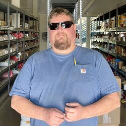 Man with blonde hair, sunglasses and a blue t-shirt with a pencil in his pocket 